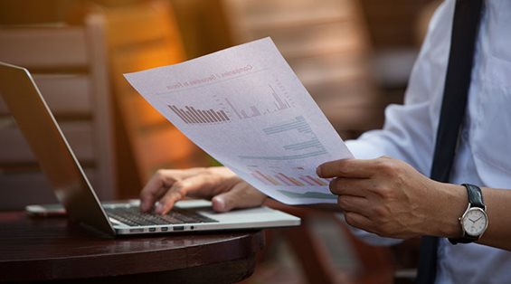 Man Typing Printed Sheet up on Laptop